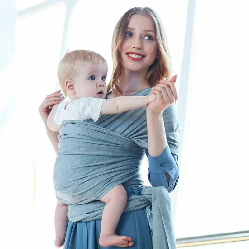 A baby sling wrap carrier with a sleeping infant inside, worn by an adult with one hand supporting the baby's head.