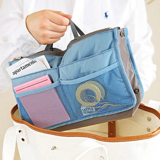 A compact bag organiser insert in blue with multiple compartments, shown being held by a hand.