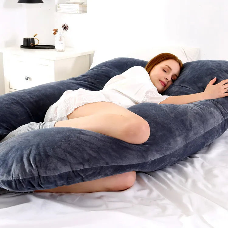 A pregnant woman lying on a blue pregnancy bump support pillow with a solid pattern.