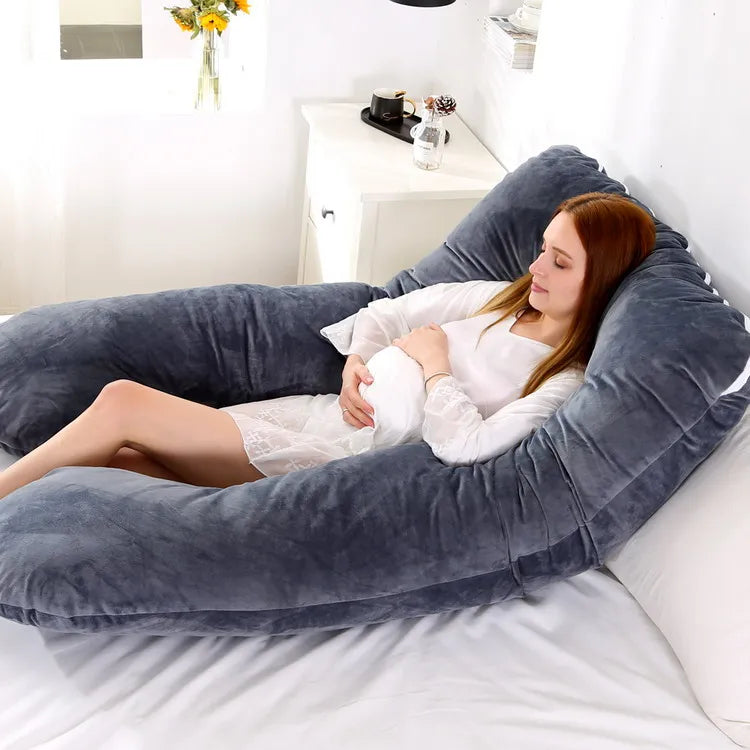 A pregnant woman lying on a blue pregnancy bump support pillow with a solid pattern.