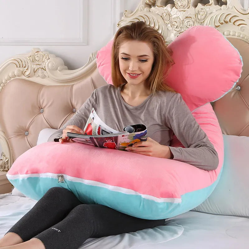 A pregnant woman lying on a pink / blue pregnancy bump support pillow with a solid pattern.