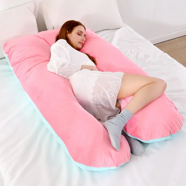 A pregnant woman lying on a pink / blue pregnancy bump support pillow with a solid pattern.