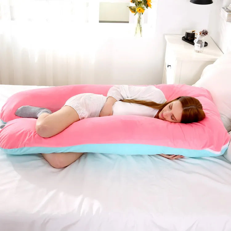 A pregnant woman lying on a pink / blue pregnancy bump support pillow with a solid pattern.