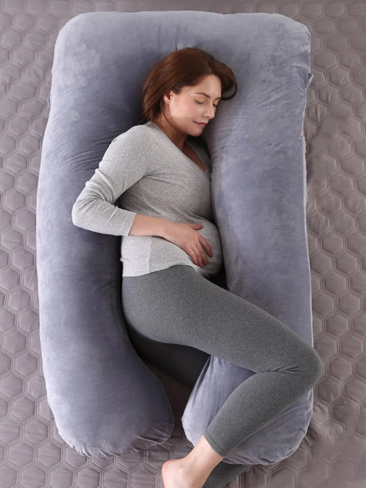 A pregnant woman lying on a light gray pregnancy bump support pillow with a solid pattern.